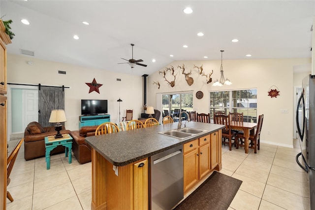 kitchen with sink, a barn door, a center island with sink, ceiling fan with notable chandelier, and appliances with stainless steel finishes