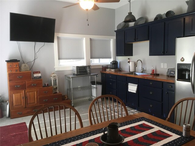 kitchen featuring stainless steel refrigerator with ice dispenser, ceiling fan, sink, blue cabinetry, and butcher block counters