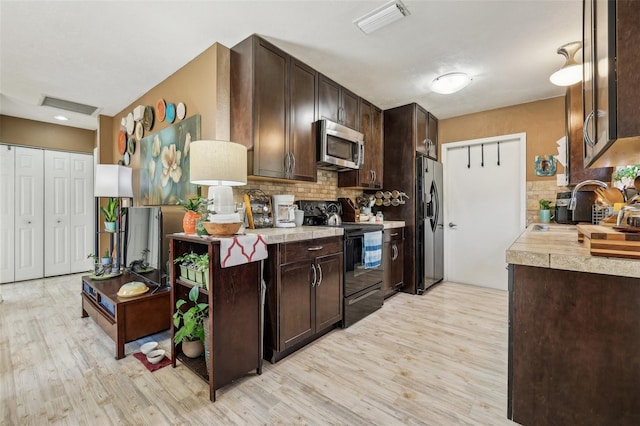 kitchen with backsplash, dark brown cabinets, stainless steel appliances, and light hardwood / wood-style floors