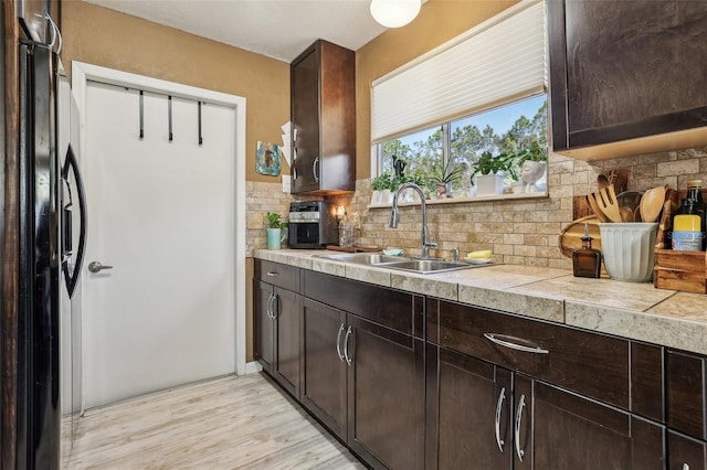 kitchen with dark brown cabinets, black refrigerator, sink, and backsplash