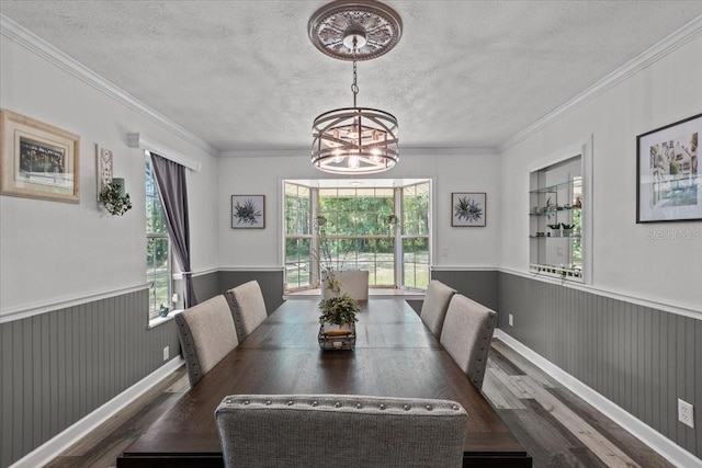 dining space with a textured ceiling, dark wood-type flooring, crown molding, and an inviting chandelier