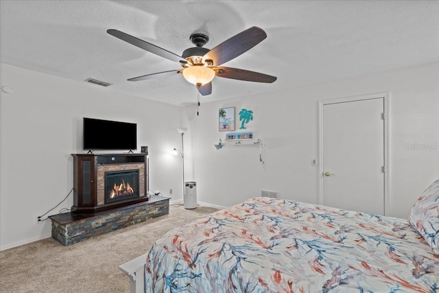 bedroom featuring ceiling fan, a fireplace, light carpet, and a textured ceiling