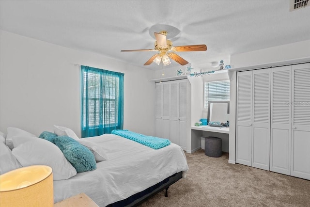 carpeted bedroom with ceiling fan, multiple windows, and multiple closets