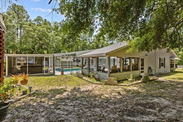 rear view of house with glass enclosure and a pool with hot tub