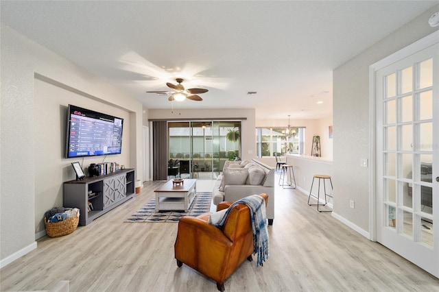 living room featuring ceiling fan with notable chandelier and light wood-type flooring