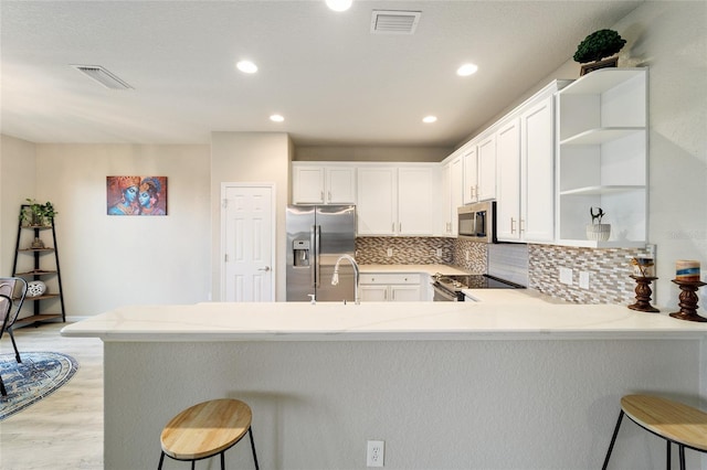 kitchen featuring kitchen peninsula, appliances with stainless steel finishes, decorative backsplash, a kitchen breakfast bar, and white cabinets