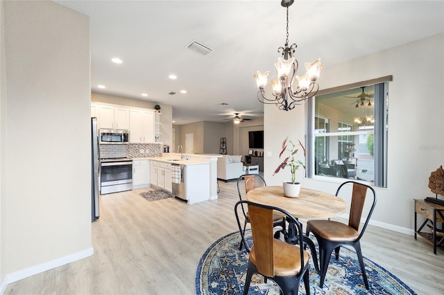 dining space featuring ceiling fan with notable chandelier, sink, and light hardwood / wood-style flooring