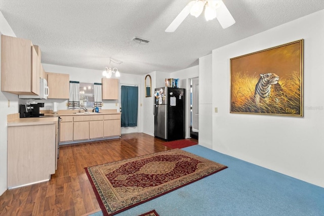 kitchen with stainless steel refrigerator, light brown cabinets, ceiling fan with notable chandelier, and a textured ceiling