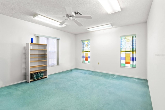 carpeted empty room with ceiling fan, a textured ceiling, and a wealth of natural light