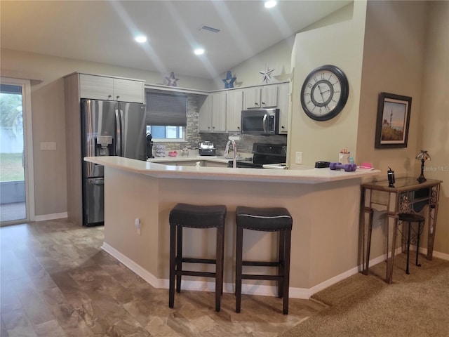 kitchen with a kitchen bar, kitchen peninsula, stainless steel fridge, and lofted ceiling