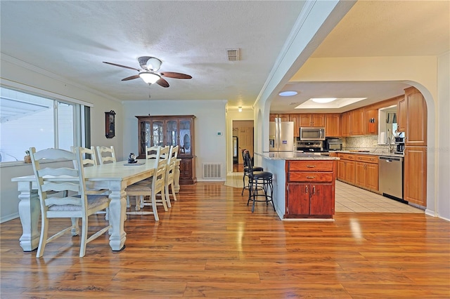 kitchen featuring ceiling fan, a center island, backsplash, a breakfast bar, and appliances with stainless steel finishes