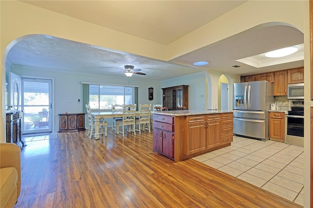 kitchen with decorative backsplash, stainless steel appliances, ceiling fan, light hardwood / wood-style flooring, and a kitchen island