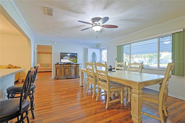 dining area featuring a textured ceiling, ceiling fan, wood-type flooring, and crown molding