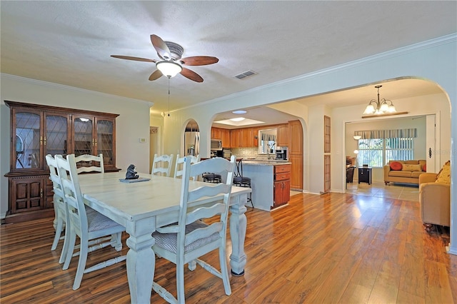 dining space featuring a textured ceiling, ceiling fan with notable chandelier, ornamental molding, and hardwood / wood-style floors