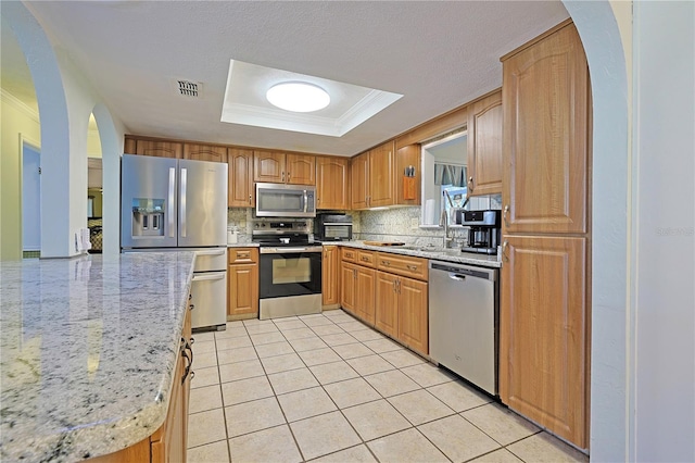 kitchen with stainless steel appliances, tasteful backsplash, a tray ceiling, light tile patterned floors, and ornamental molding