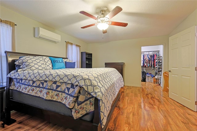 bedroom featuring a walk in closet, hardwood / wood-style flooring, ceiling fan, a wall unit AC, and a closet