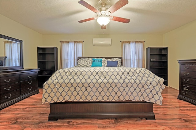 bedroom with hardwood / wood-style flooring, ceiling fan, an AC wall unit, and a textured ceiling