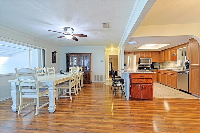 kitchen with crown molding, decorative backsplash, light wood-type flooring, appliances with stainless steel finishes, and a kitchen island