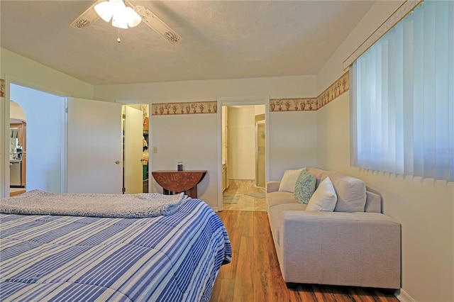 bedroom featuring connected bathroom, ceiling fan, a walk in closet, a closet, and hardwood / wood-style flooring