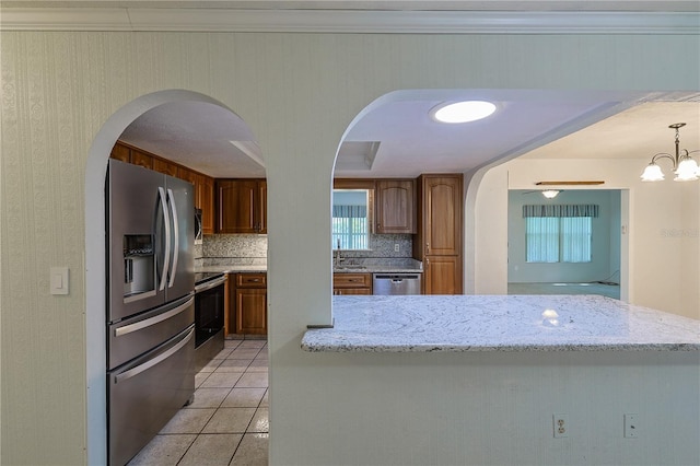 10185 SE 175th Ln, Summerfield, FL 34491 - kitchen with stainless steel appliances, arched walkways, tasteful backsplash, brown cabinets, and light tile patterned flooring