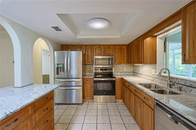 10185 SE 175th Ln, Summerfield, FL 34491 - kitchen featuring stainless steel appliances, a sink, a raised ceiling, backsplash, and brown cabinets