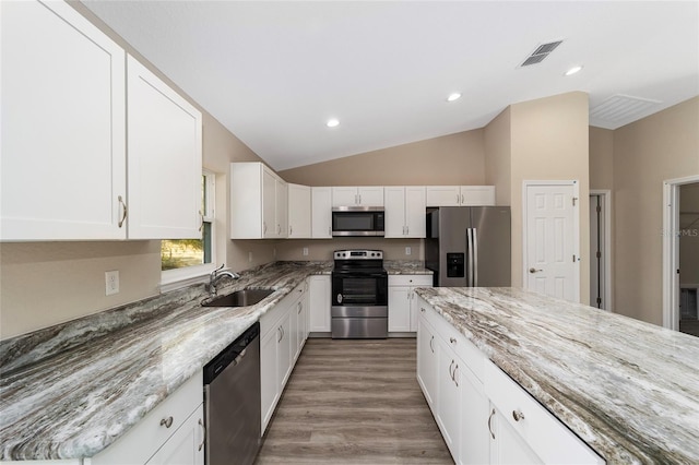 kitchen with appliances with stainless steel finishes, light stone counters, sink, white cabinetry, and lofted ceiling