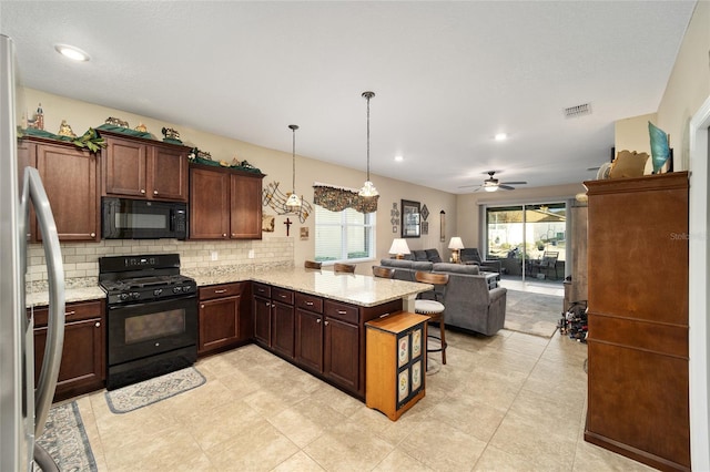 kitchen with pendant lighting, black appliances, ceiling fan with notable chandelier, a kitchen breakfast bar, and kitchen peninsula