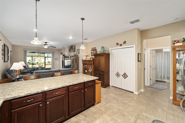 kitchen with pendant lighting, dark brown cabinets, light stone counters, and ceiling fan