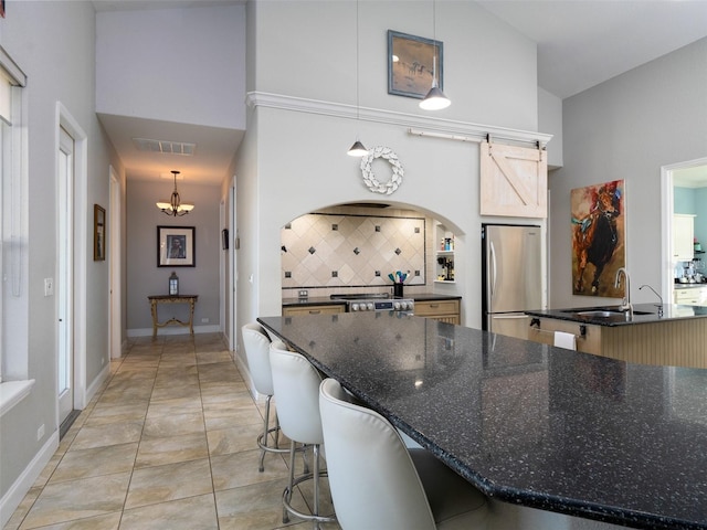 kitchen featuring a kitchen breakfast bar, backsplash, sink, pendant lighting, and stainless steel refrigerator