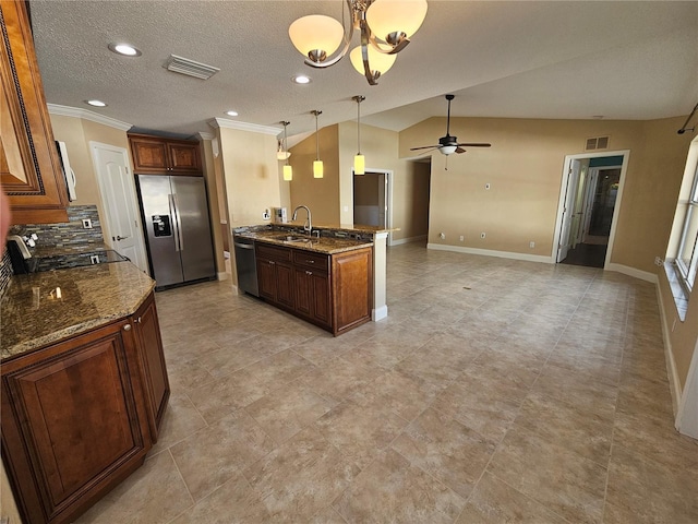 kitchen featuring vaulted ceiling, decorative light fixtures, a center island with sink, ceiling fan with notable chandelier, and appliances with stainless steel finishes