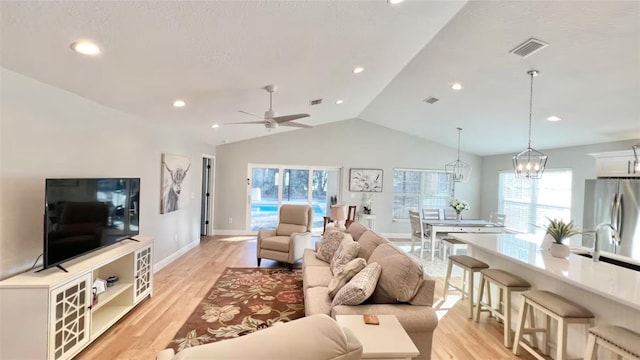 living room featuring light wood-type flooring, lofted ceiling, and ceiling fan with notable chandelier