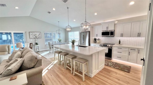 kitchen with a kitchen island with sink, white cabinets, decorative backsplash, and stainless steel appliances