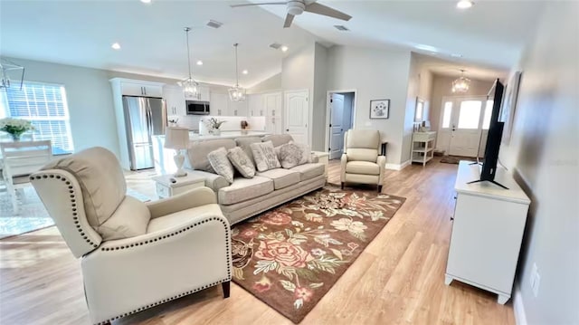 living room with ceiling fan with notable chandelier, light hardwood / wood-style floors, and high vaulted ceiling