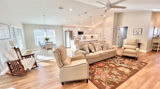 living room featuring vaulted ceiling, ceiling fan with notable chandelier, and light hardwood / wood-style floors