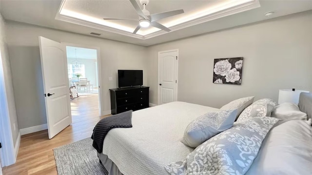 bedroom with ceiling fan, ornamental molding, a raised ceiling, and light wood-type flooring