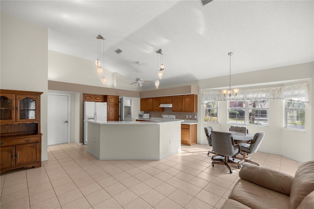 kitchen featuring ceiling fan with notable chandelier, vaulted ceiling, light tile patterned floors, decorative light fixtures, and a kitchen island