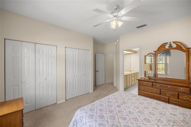 bedroom featuring connected bathroom, ceiling fan, light carpet, and two closets