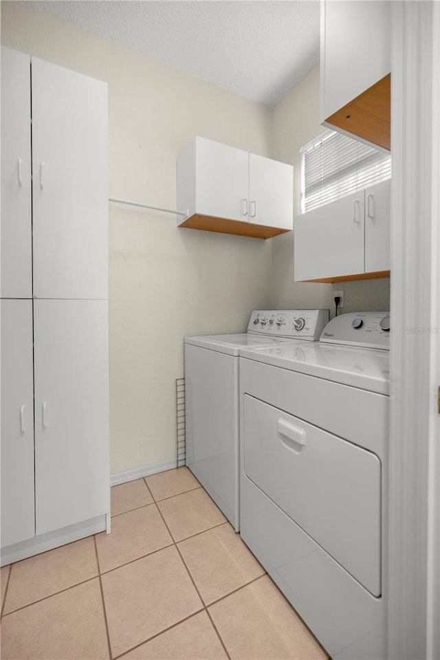 laundry room featuring cabinets, independent washer and dryer, a textured ceiling, and light tile patterned floors