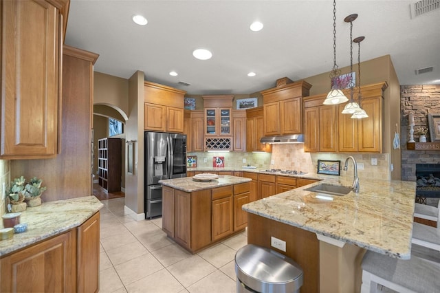 kitchen featuring kitchen peninsula, light stone countertops, stainless steel appliances, sink, and pendant lighting