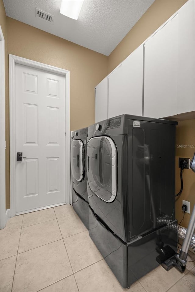 laundry room featuring cabinets, light tile patterned floors, a textured ceiling, and washing machine and clothes dryer