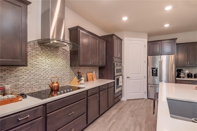 kitchen featuring appliances with stainless steel finishes, backsplash, dark brown cabinetry, and wall chimney range hood