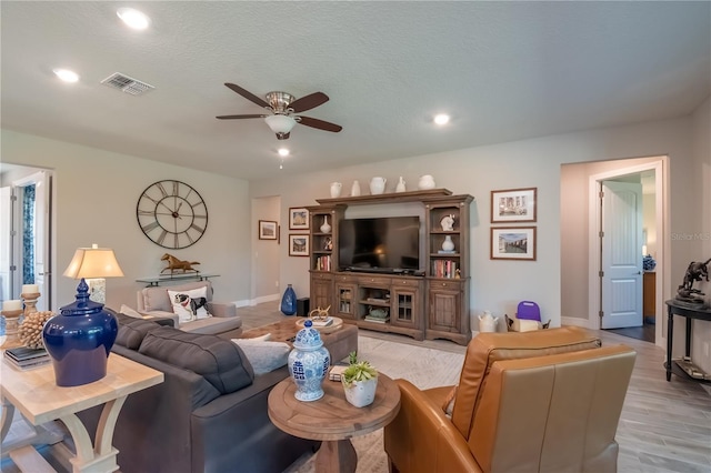 living room with ceiling fan, a textured ceiling, and light wood-type flooring