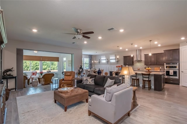 living room featuring ceiling fan with notable chandelier and light hardwood / wood-style flooring