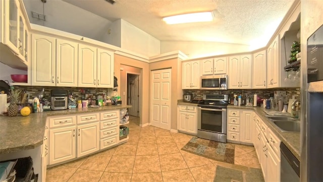 kitchen featuring light tile patterned floors, stainless steel appliances, a sink, vaulted ceiling, and decorative backsplash