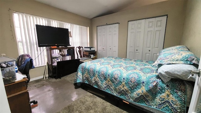 bedroom featuring multiple closets, lofted ceiling, and concrete flooring