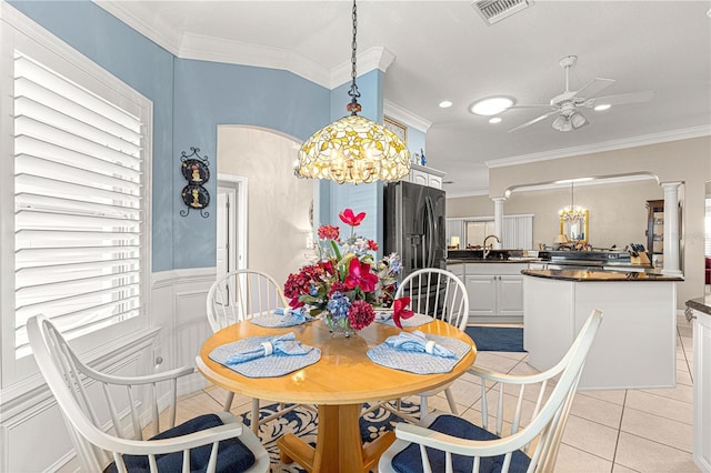 tiled dining area featuring ceiling fan with notable chandelier, decorative columns, crown molding, and sink