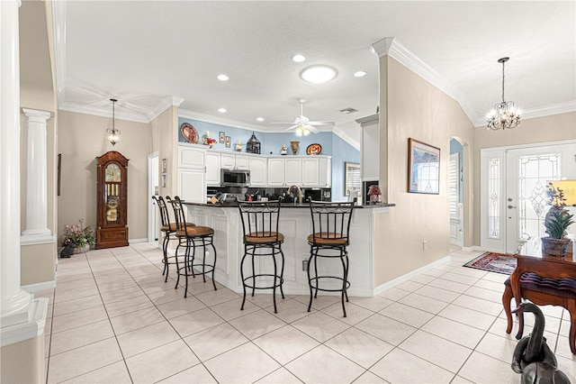 kitchen featuring ceiling fan with notable chandelier, kitchen peninsula, a kitchen bar, white cabinetry, and decorative columns