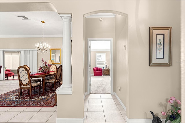 corridor featuring decorative columns, light tile patterned flooring, a chandelier, and ornamental molding