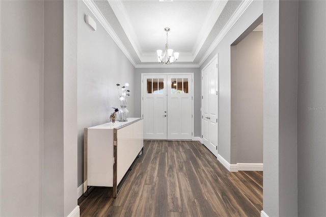 entryway with crown molding, a raised ceiling, dark wood-type flooring, and a chandelier