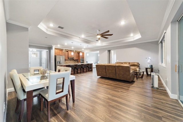 dining space with a raised ceiling, crown molding, dark hardwood / wood-style flooring, and ceiling fan